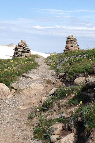 Rocky trail splitting cairns with snowfield in the background